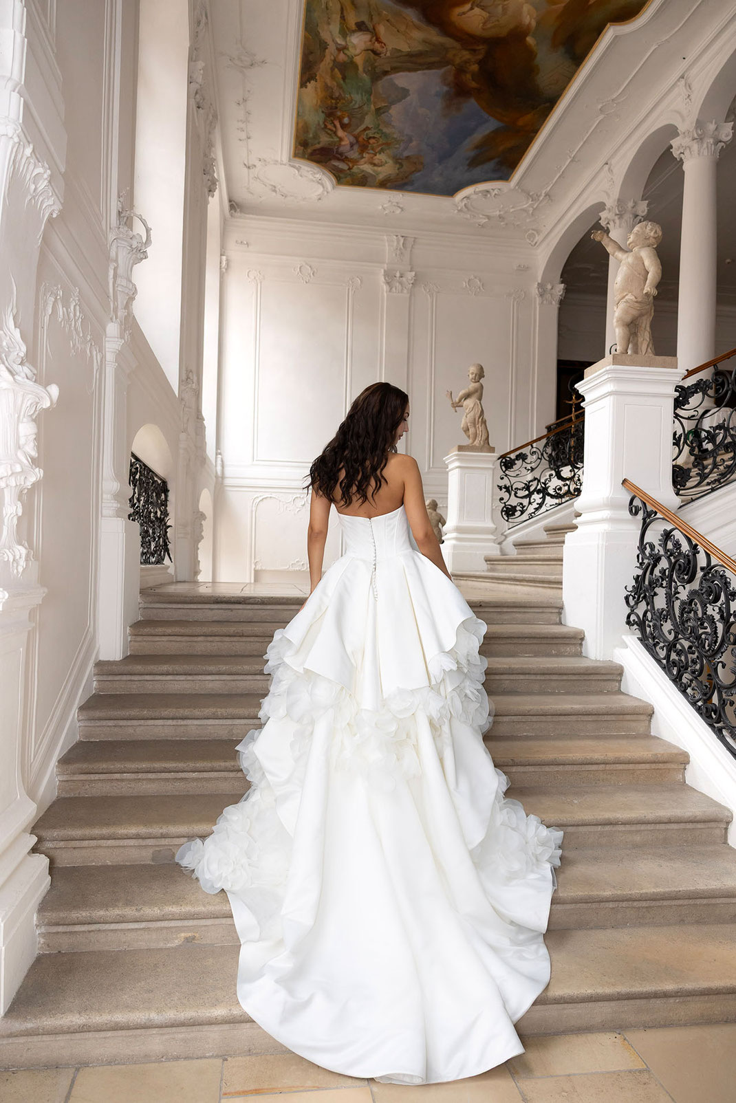 Frau mit Brautkleid von Amo & Luv geht eine Treppe in einer Altstadtvilla hoch