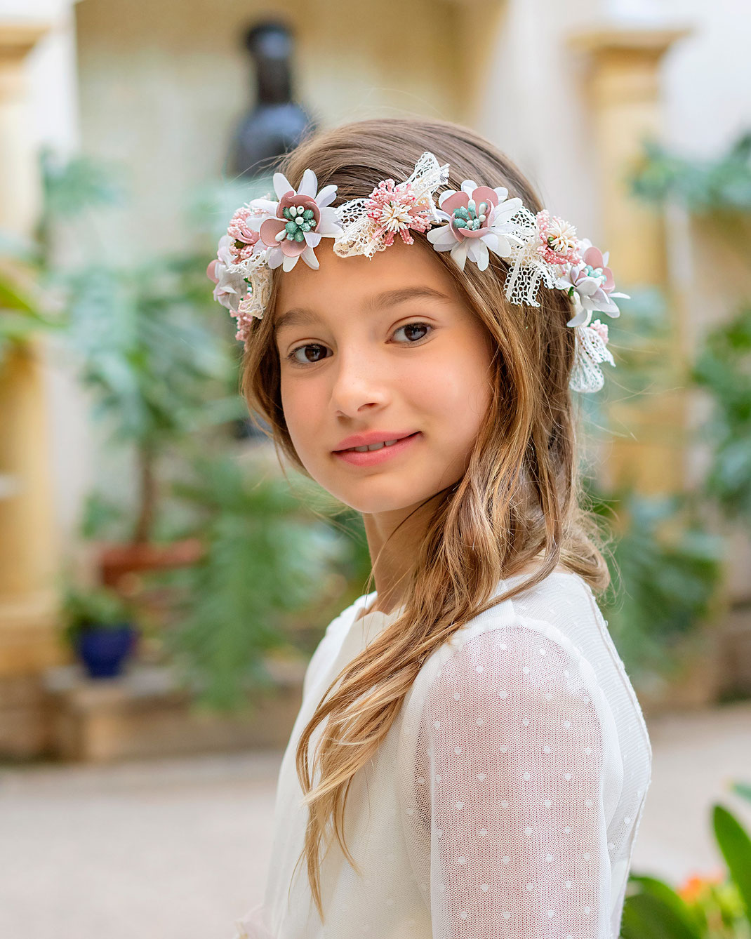 Junges Mädchen mit Haarreif trägt ein süßes Kommunionskleid aus der Aire Mini Kollektion