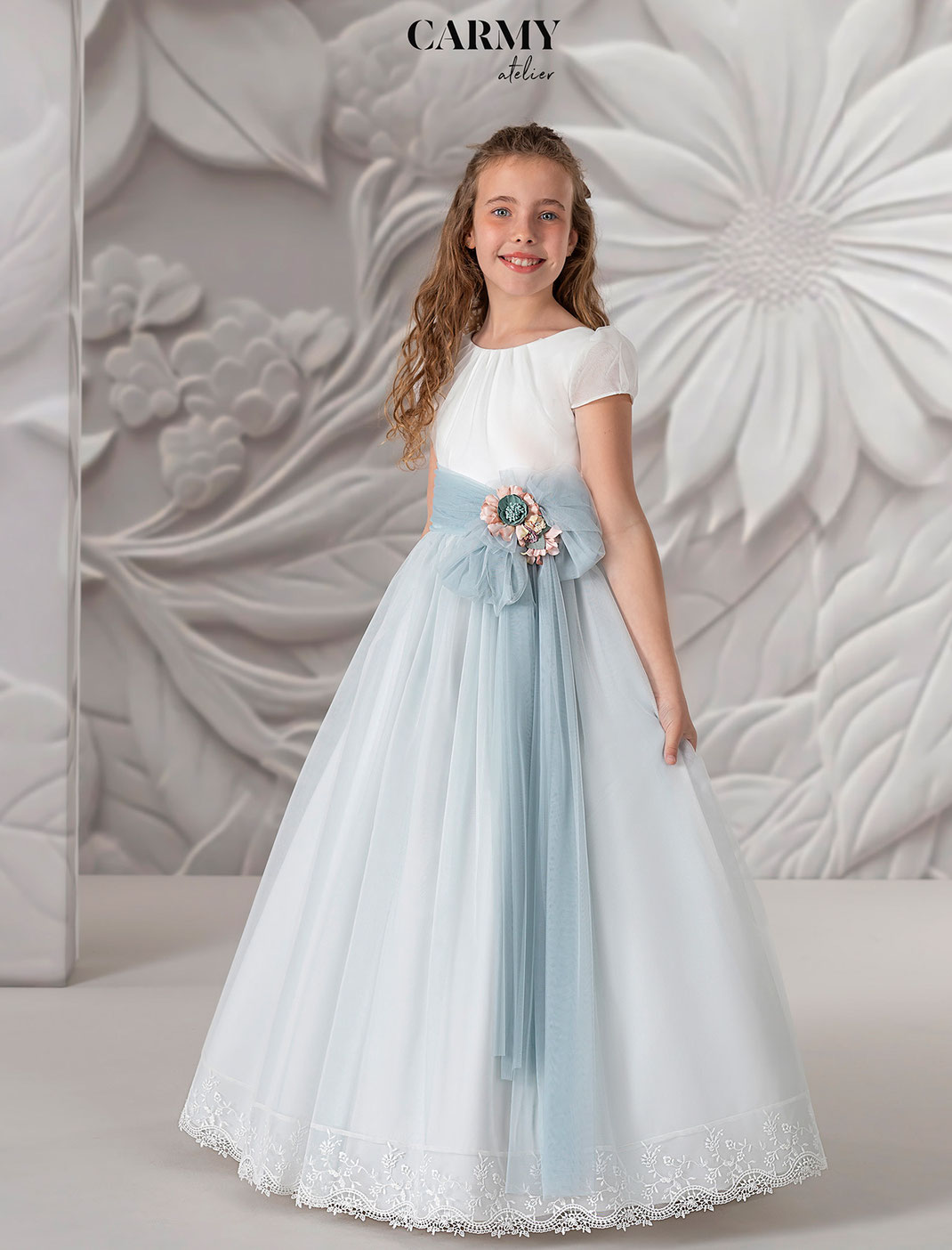 Mädchen trägt ein süßes Carmy Kommunionkleid mit blauer Schleife