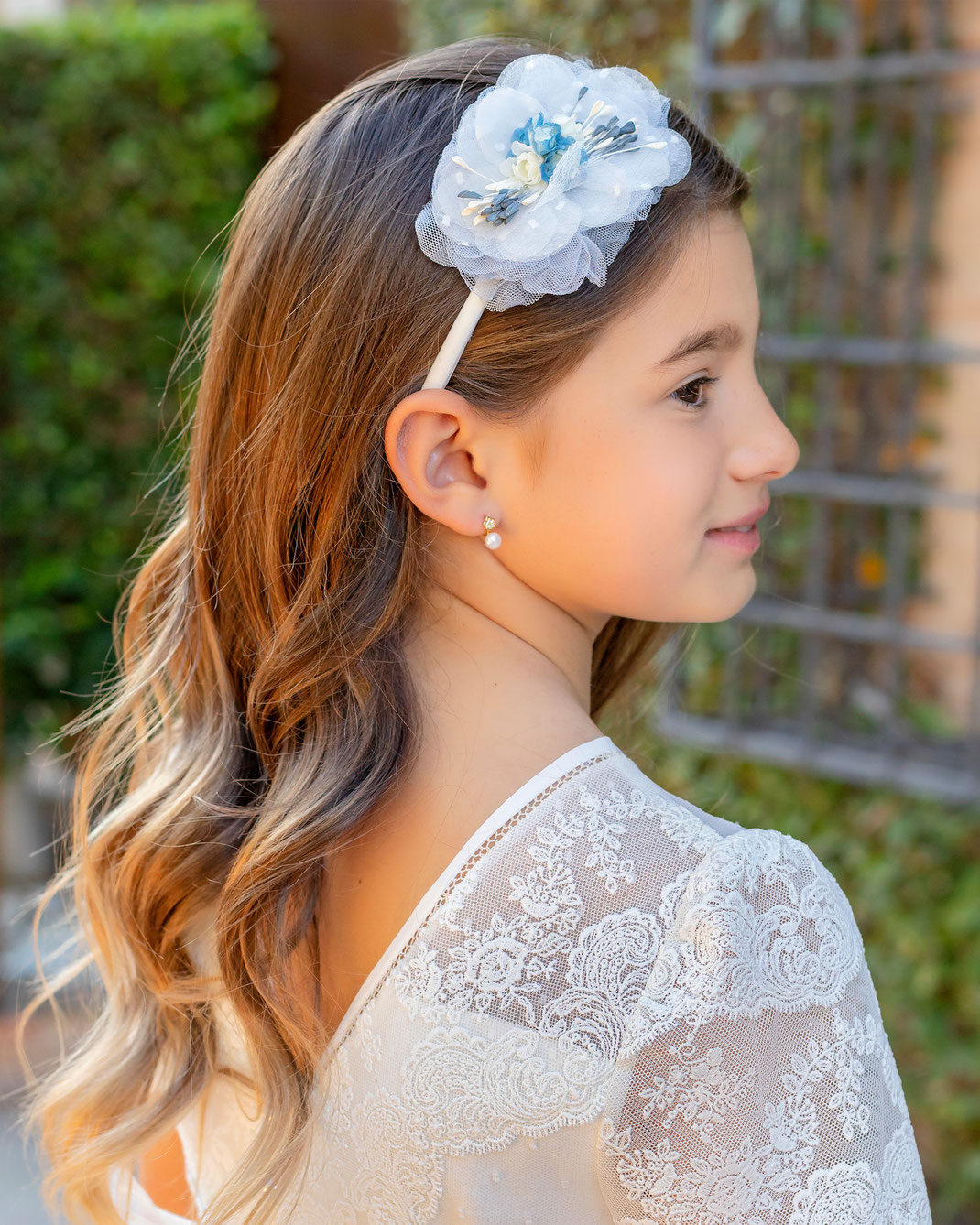 Junges Mädchen mit Haarreif trägt ein Kommunionskleid aus der Aire Mini Kollektion