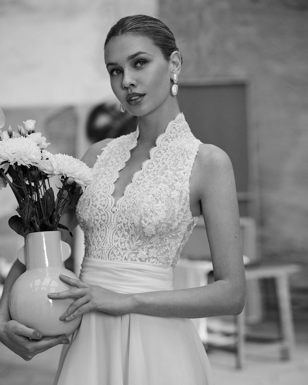 Junge Frau hält eine Blumenvase in der Hand und trägt das Brautkleid Milan aus der Aire Barcelona Kollektion 2026