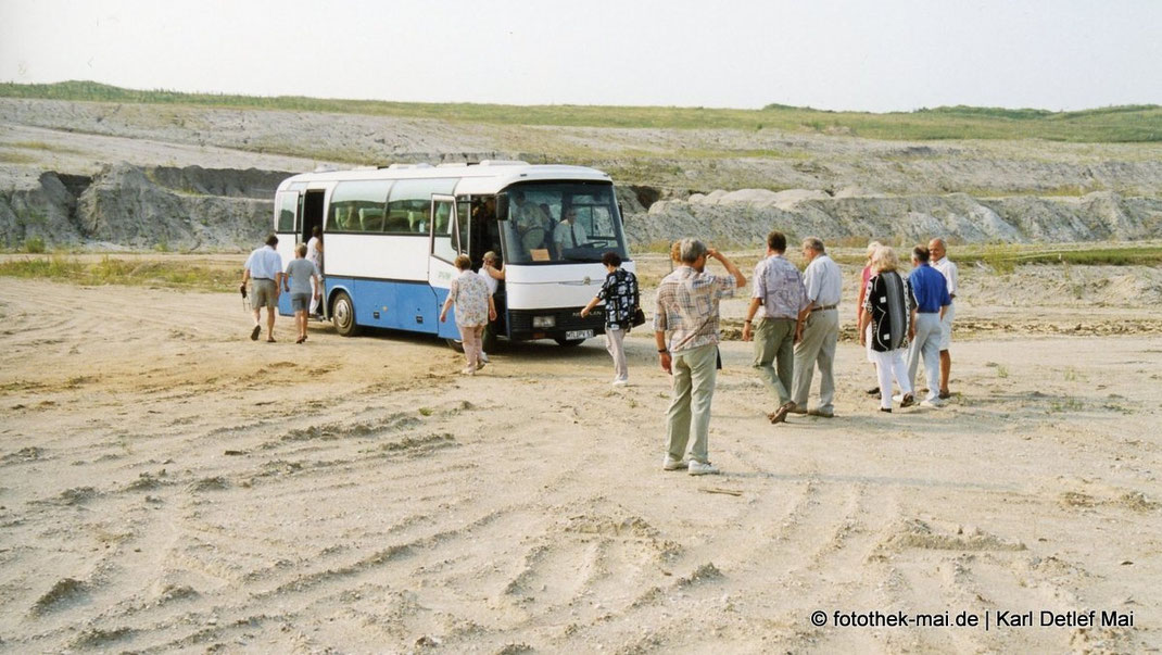 Bus im Tagebau auf Sandfläche mit Fahrgästen, die ausgestiegen sind.