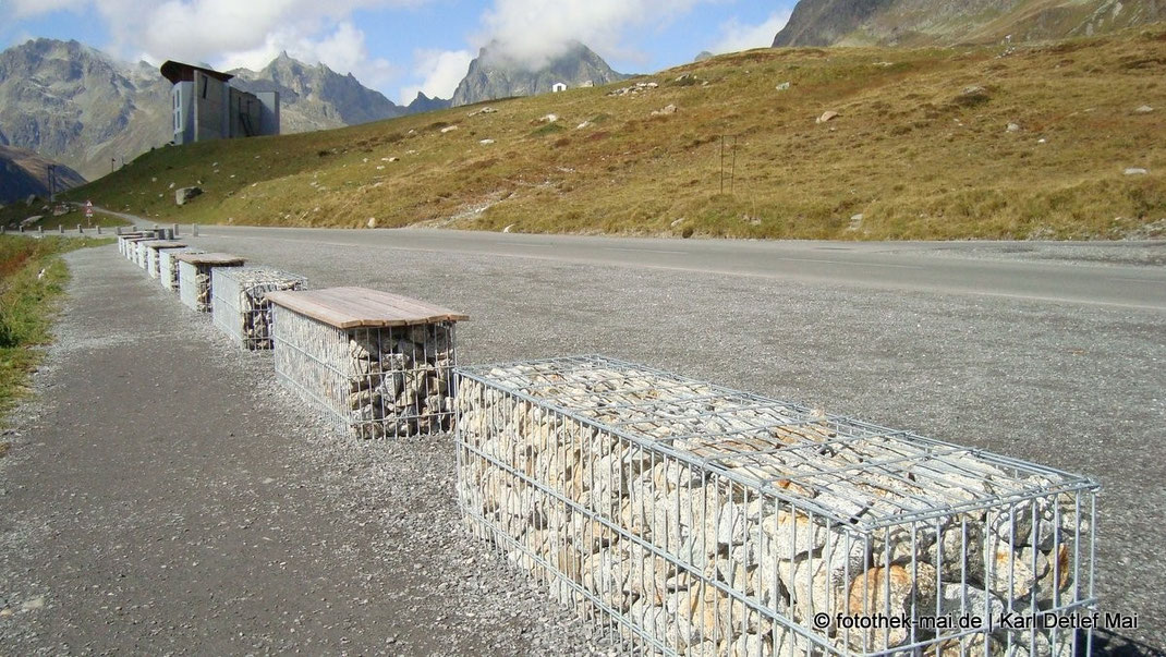 In den Alpen Österreichs entdeckt: Steine in Drahtkörben als Absperrung an der Straße, die teils als Sitzbank nutzbar sind.