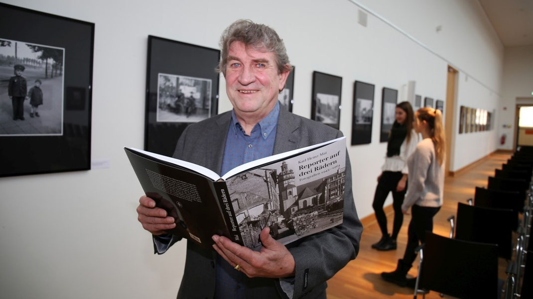 Oberlichtsaal, Portrait Karl Detlef Mai mit Bildband in der Hand - gerahmte Bilder an der Wand