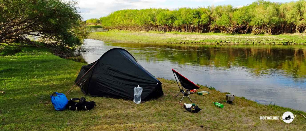 Grünes Zelt, grüne Wiese, Fluss, Bäume und Wäld, Camping Stühl, Kocher, Wasserflasche und Schutzbeutel