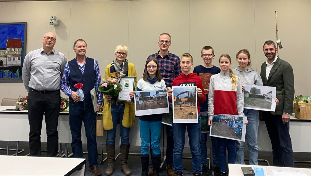 Foto v.l.n.r.: Die Kahler Steinkäuze Alexius Wack, Martina Wack, Vanessa, Martin Schäfer, Tristan, Benno, Theresa und Elisabeth, umrahmt von Udo Hammer (links, 2. Bürgermeister von Kahl) und Landrat Dr. Alexander Legler bei der Preisverleihung 