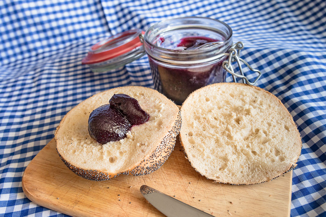 Mohnbrötchen mit rotem Weintraubengelee auf blau weiss karierter Tischdecke