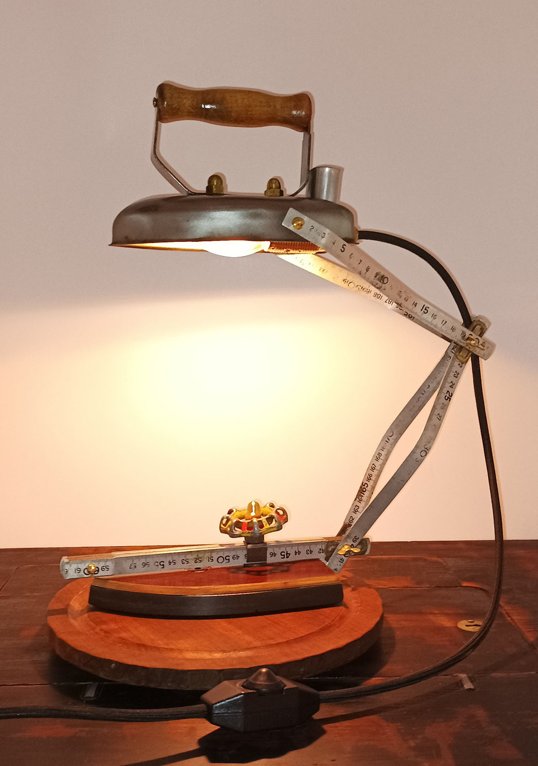 Eine Tischlampe aus einem alten Bügeleisen. Das Bügeleisen wurde zerlegt, die Heizplatte ist jetzt der Lampenfuß, und das Oberteil der Lampenschirm. Für den Lampenarm wurde ein alter Metallzollstock verwendet.