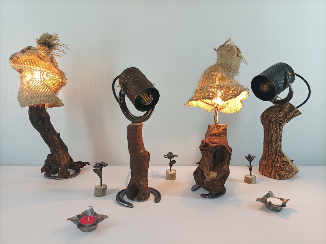 4 Tischlampen mit Baumästen als Lampenarm. 2 Lampen haben einen Lampenschirm aus einer alten Konservendose, und 2 aus altem Kaffeesack. Zwischen den Lampen stehen 3 kleine Blumen aus Schrauben und 2 Teelichthalter aus Blech, die wie Blüten aussehen.