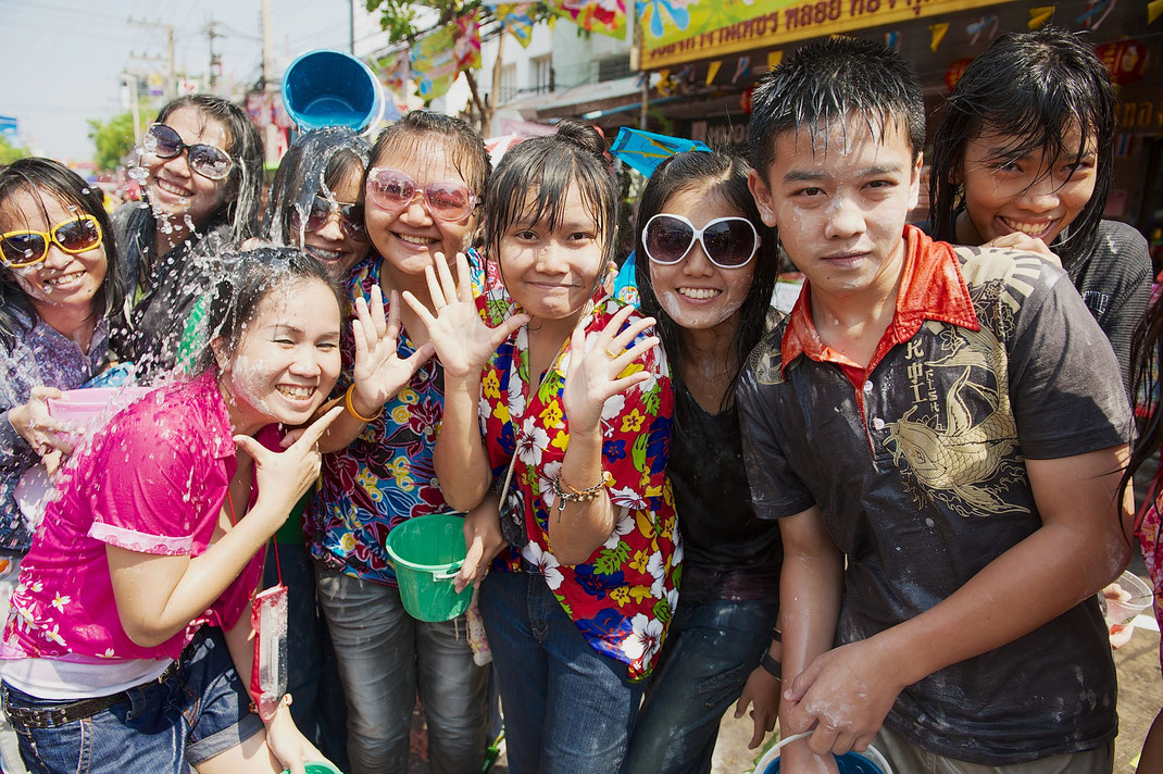 Eine Gruppe lachender junger Thailänder feiert das Songkran-Fest, ist nassgespritzt und trägt weißes Puder im Gesicht.