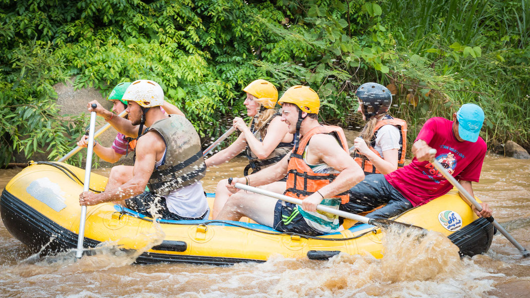 Gruppe von jungen Reisenden in einem Wildwasserboot in Kanchanaburi auf dem River Kwai