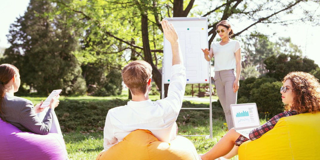 Menschen sitzen draußen auf Sitzsäcken und hören einer Präsentation am Flipchart zu.