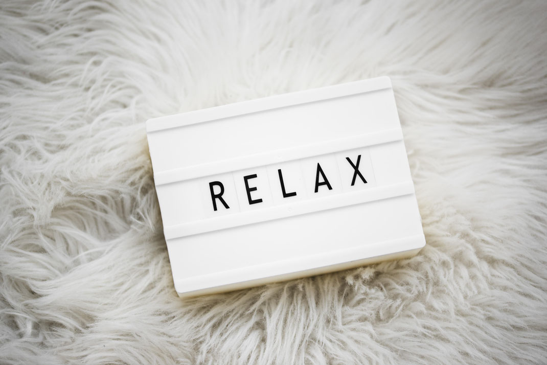 Leuchtbox mit dem Wort RELAX auf weicher weißer Flauschdecke – Symbol für Entspannung und Wohlbefinden zu Hause