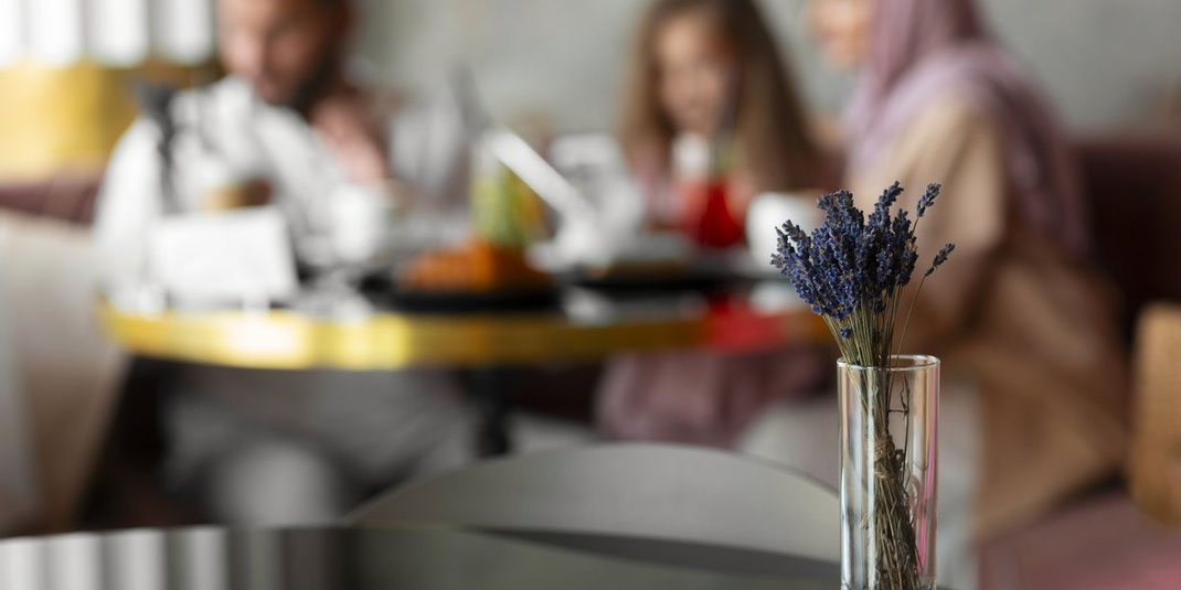 Familie sitzt gemeinsam an einem Tisch in einem Café, im Vordergrund ein Glas mit getrocknetem Lavendel.