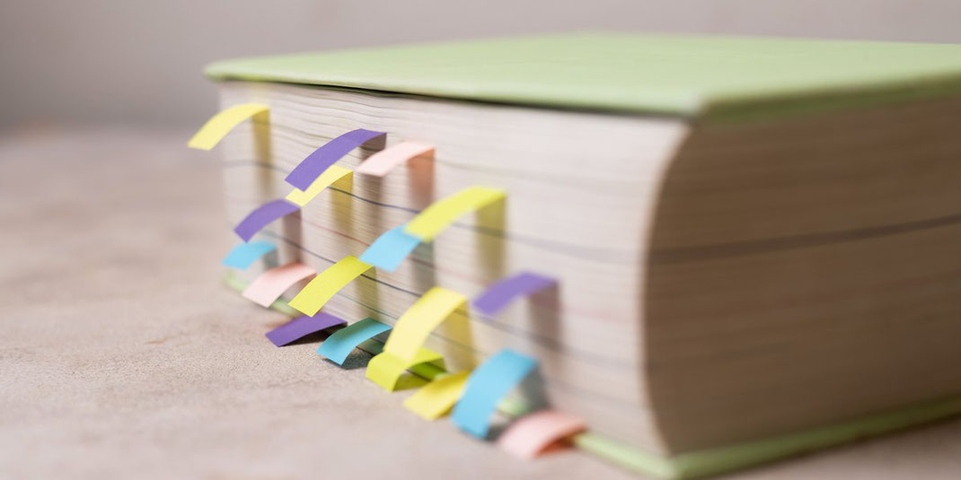 Dickes Buch mit vielen bunten Klebezetteln als Markierungen, Symbol für intensive Vorbereitung und Organisation.