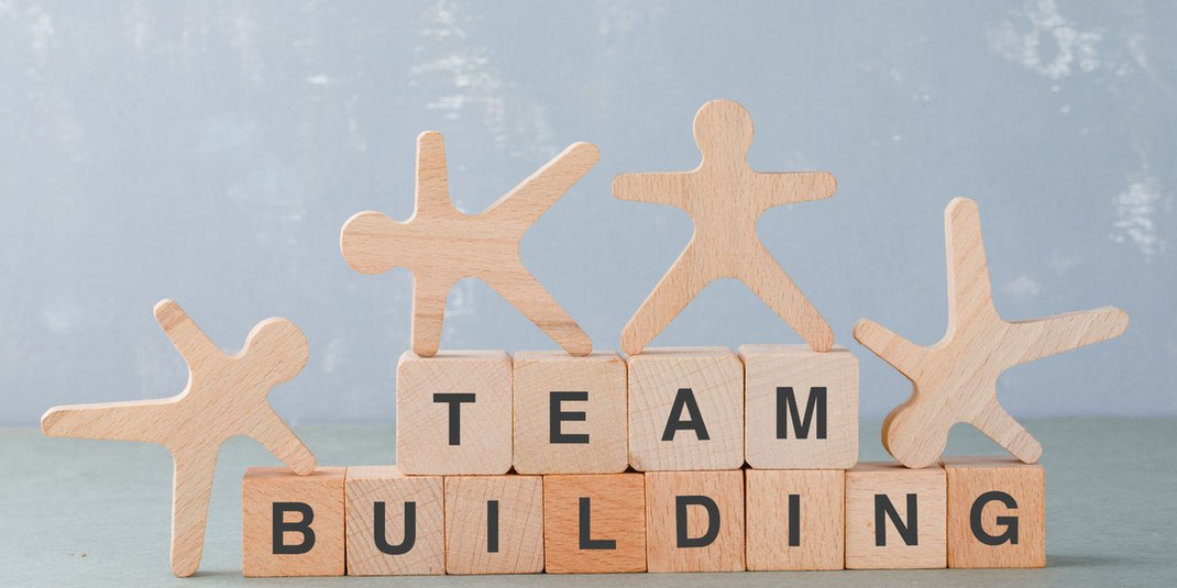 Holzklötze mit Buchstaben Team Building und Figuren symbolisieren Zusammenarbeit.