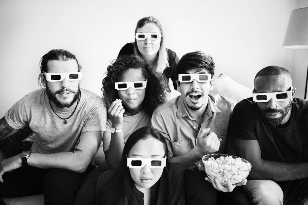 Gruppe von Freunden trägt 3D-Brillen und schaut begeistert einen Film, während sie Popcorn essen.