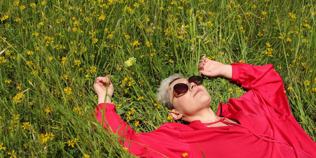Frau mit rotem Kleid und Sonnenbrille liegt entspannt auf einer Blumenwiese.