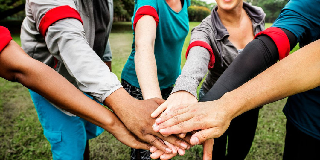 Verschiedenes Team legt im Freien die Hände übereinander als Zeichen von Zusammenhalt