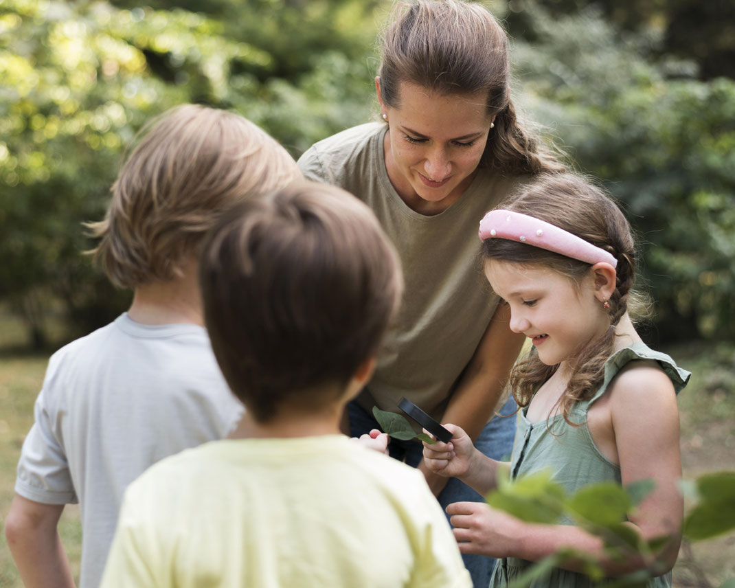 Lehrerin erkundet mit Kindern Blätter in der Natur – Naturpädagogik und Umweltbildung im Grünen erleben