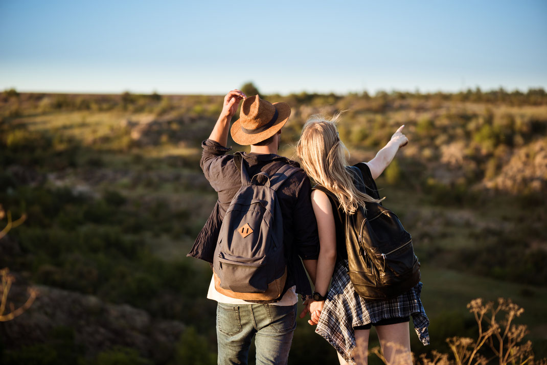 Junges Paar mit Rucksäcken hält Händchen und blickt in die Ferne – Natur erleben, Abenteuerlust und Wanderausflug im Sommer