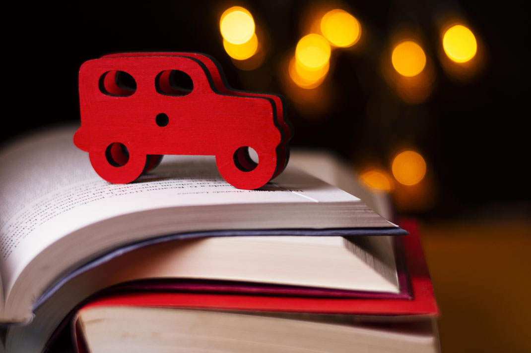 Rotes Holzauto steht auf aufgeschlagenem Buch vor Lichterkulisse – Symbol für Fantasie, Reiselust und kindliche Abenteuer in Geschichten