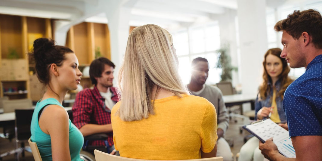 Gruppe junger Menschen sitzt in einem modernen Büro im Stuhlkreis und diskutiert gemeinsam, symbolisiert Teamarbeit und Austausch.