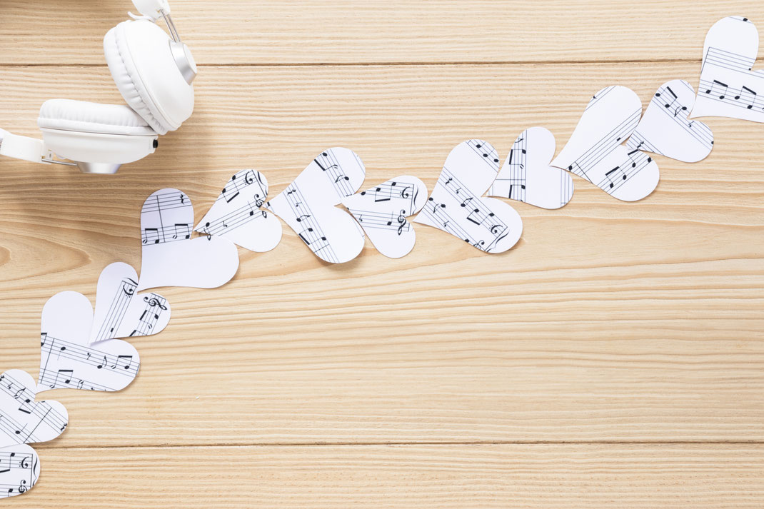 Weiße Kopfhörer neben Papierherzen aus Notenblättern auf Holz – Musikliebe, kreative Dekoration und musikalische Inspiration