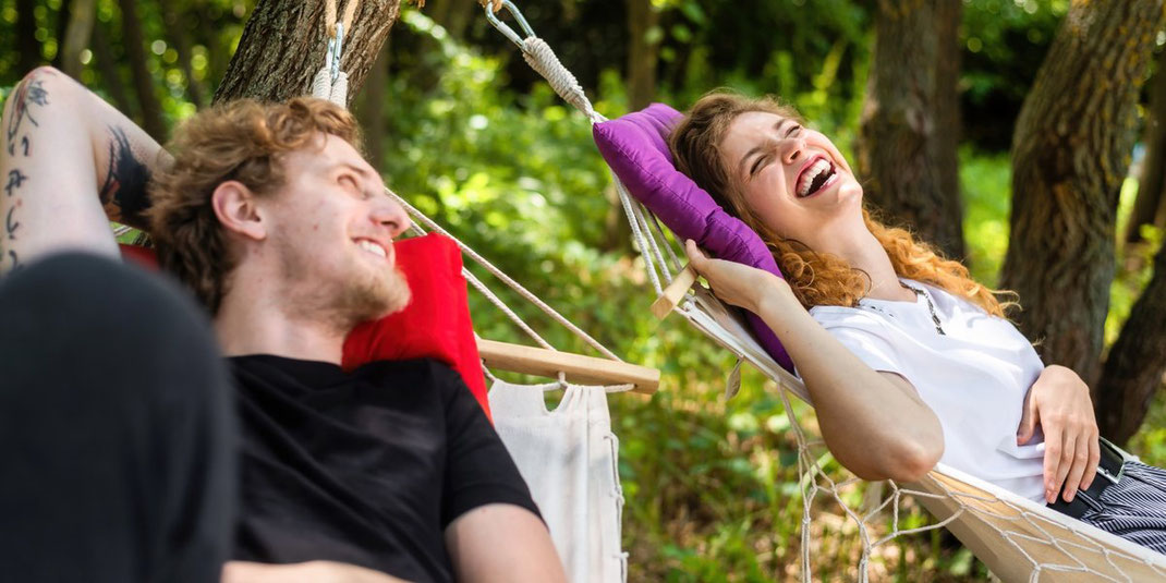 Junges Paar entspannt lachend zusammen in einer Hängematte im Grünen