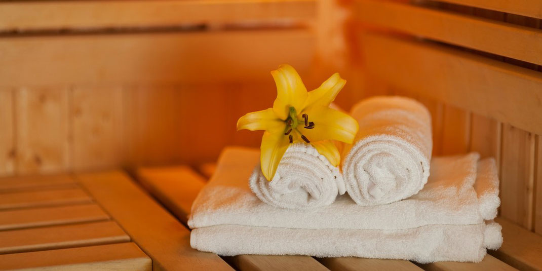 Weiße Handtücher mit gelber Lilie auf einer Bank in der Sauna.