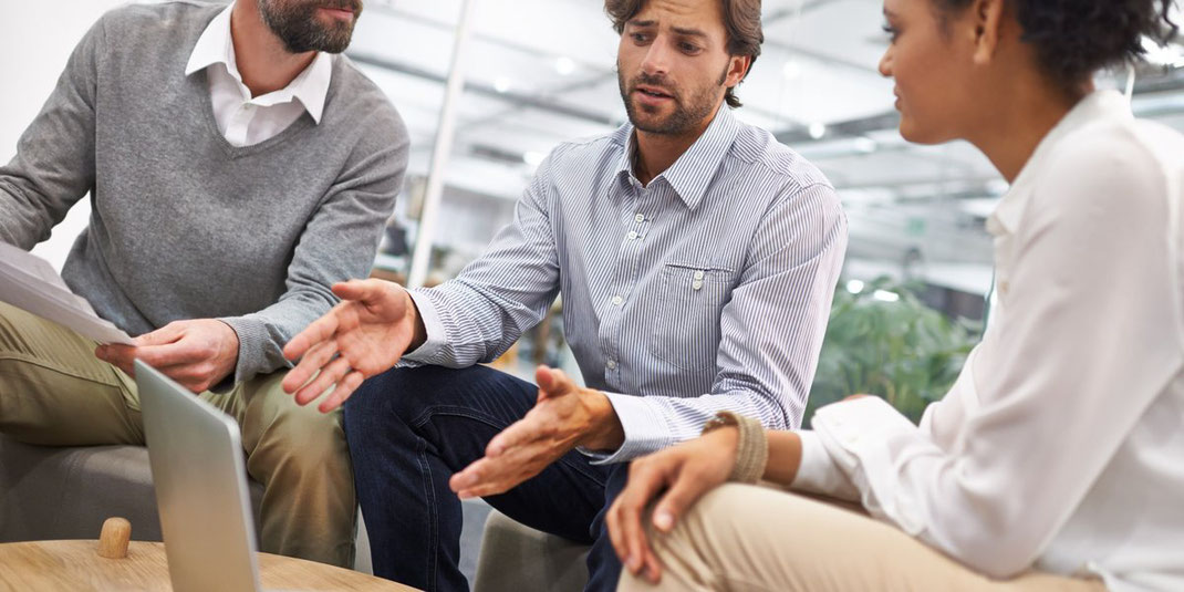 Drei Personen in Business-Kleidung diskutieren konzentriert an einem Laptop in einem modernen Büro