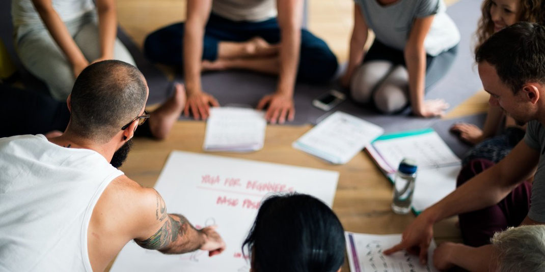Gruppe von Menschen sitzt auf dem Boden im Kreis und diskutiert über Yoga-Übungen.