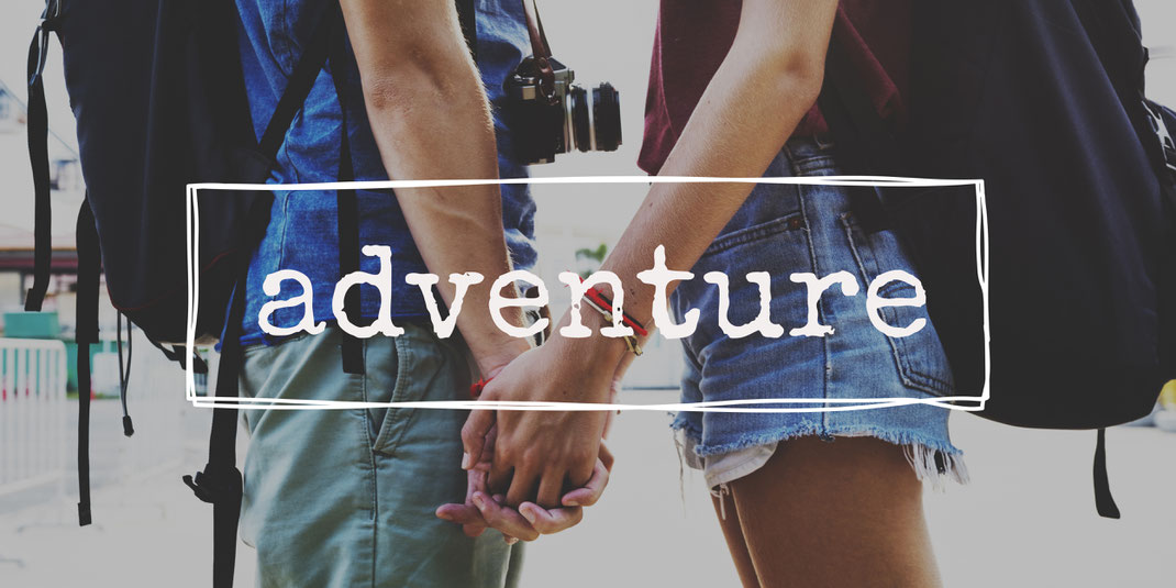 Nahaufnahme eines Händchen haltenden Paars mit Rucksäcken und dem Schriftzug ‚adventure‘ – Reiseinspiration und gemeinsame Entdeckerlust