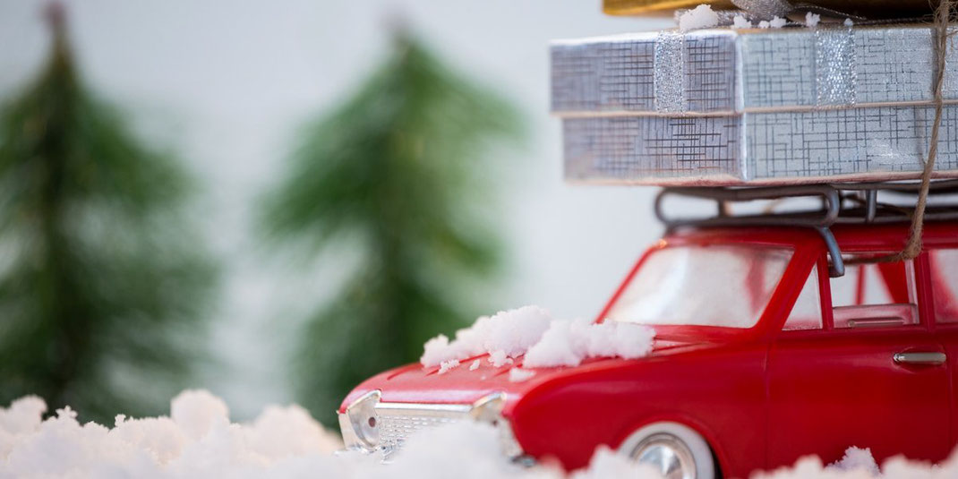 Rotes Spielzeugauto im Schnee trägt bunte Geschenkboxen auf dem Dachträger.