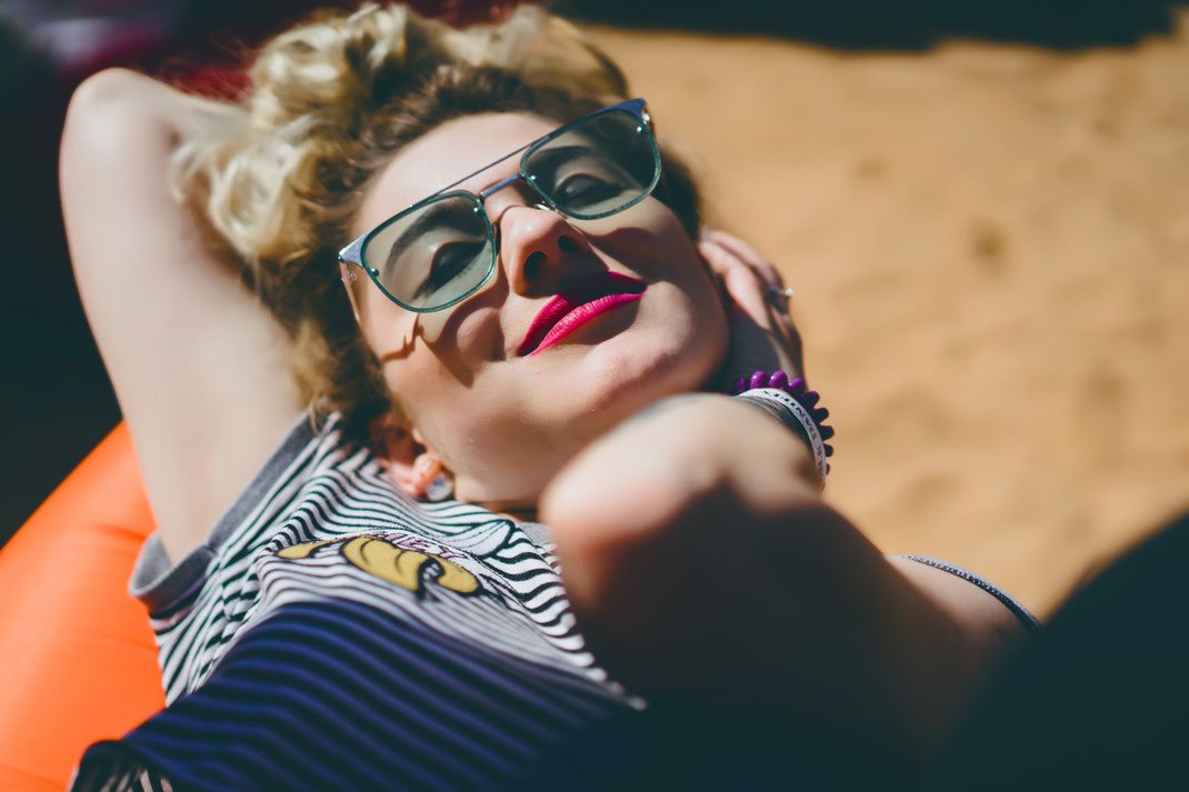 Junge Frau mit Sonnenbrille und knalligem Lippenstift liegt entspannt in der Sonne und genießt den Moment – Nahaufnahme mit sommerlicher Stimmung.