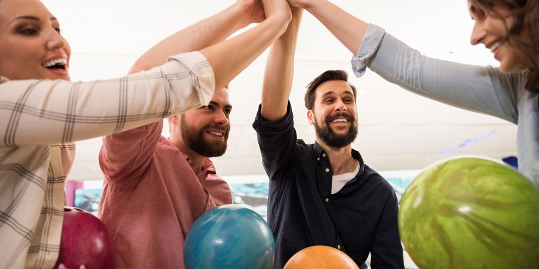 Gruppe junger Freunde mit Bowlingkugeln feiert gemeinsam einen Erfolg mit High-Five.