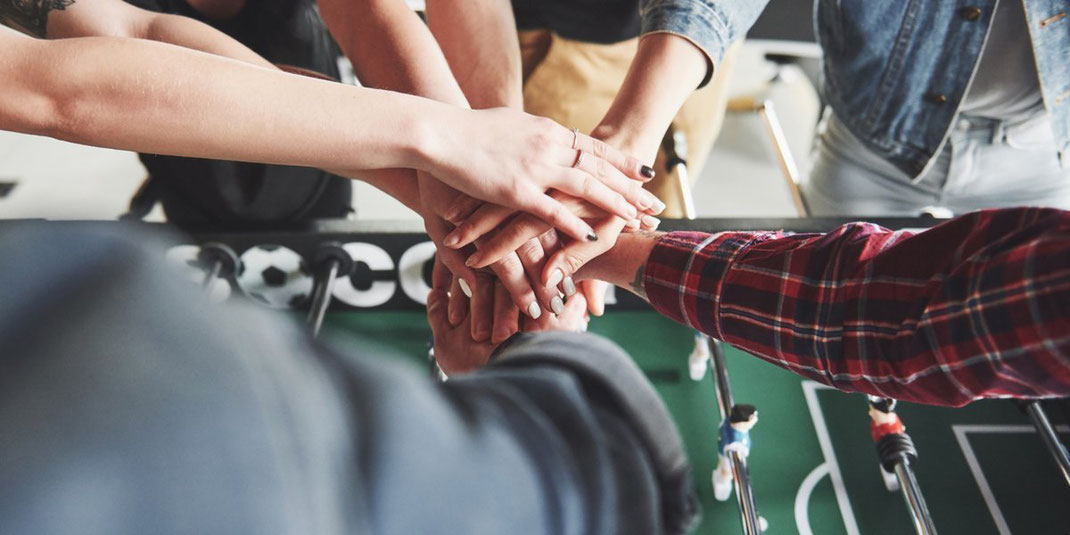 Mehrere Hände verschiedener Personen liegen übereinander als Symbol für Teamwork