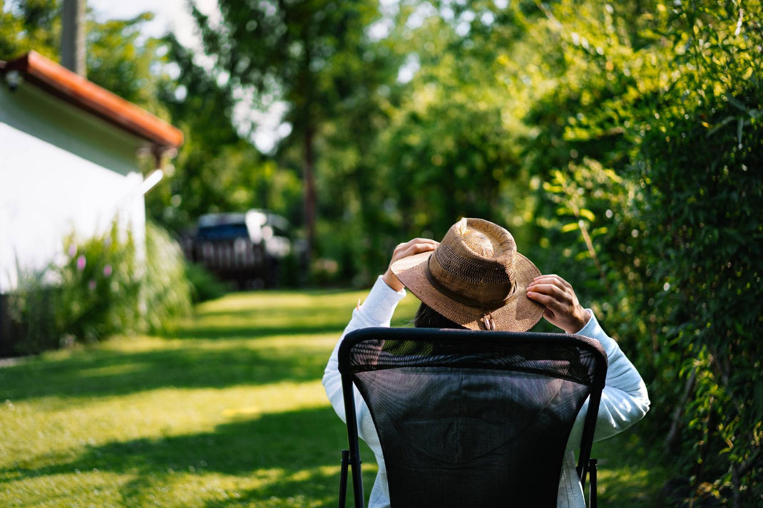 Person mit Strohhut entspannt im Gartenstuhl an einem sonnigen Tag.