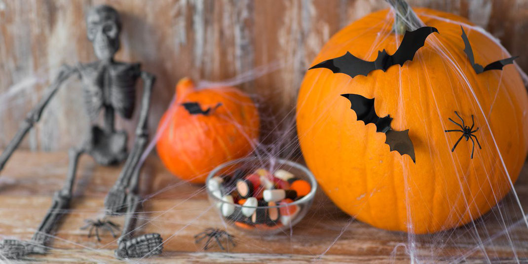 Halloween-Dekoration mit geschnitzten Kürbissen, Spinnweben, Fledermausfiguren, Skelett und Schale voller Süßigkeiten