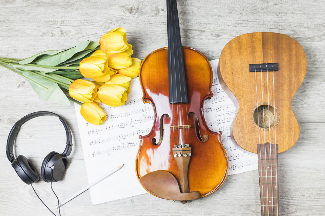 Frühlingshaftes Musikstillleben mit Geige, Gitarre, gelben Tulpen und Kopfhörern auf Notenblatt – Musikalität trifft Ästhetik