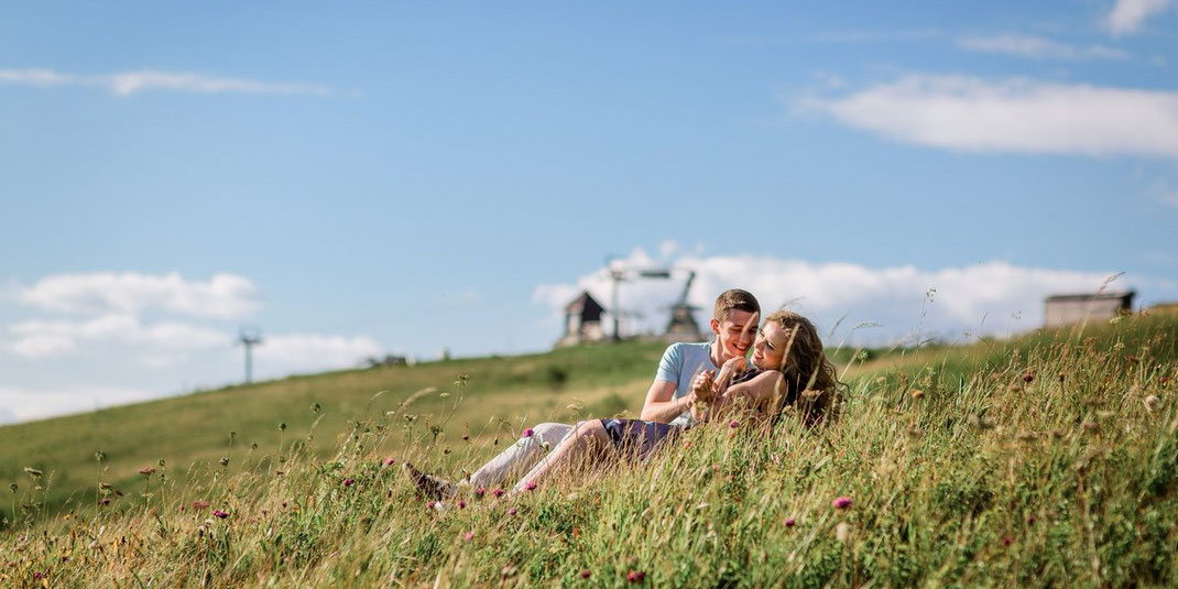 Paar liegt Arm in Arm auf einer Blumenwiese mit weitem Blick in die Landschaft