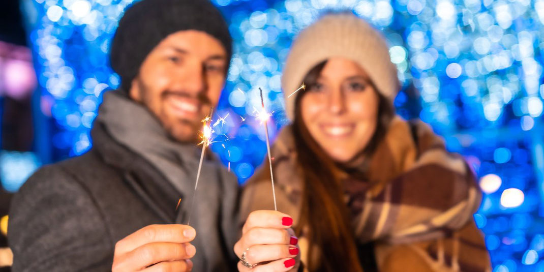 Junges Paar hält Wunderkerzen in den Händen vor festlicher Lichterdekoration.