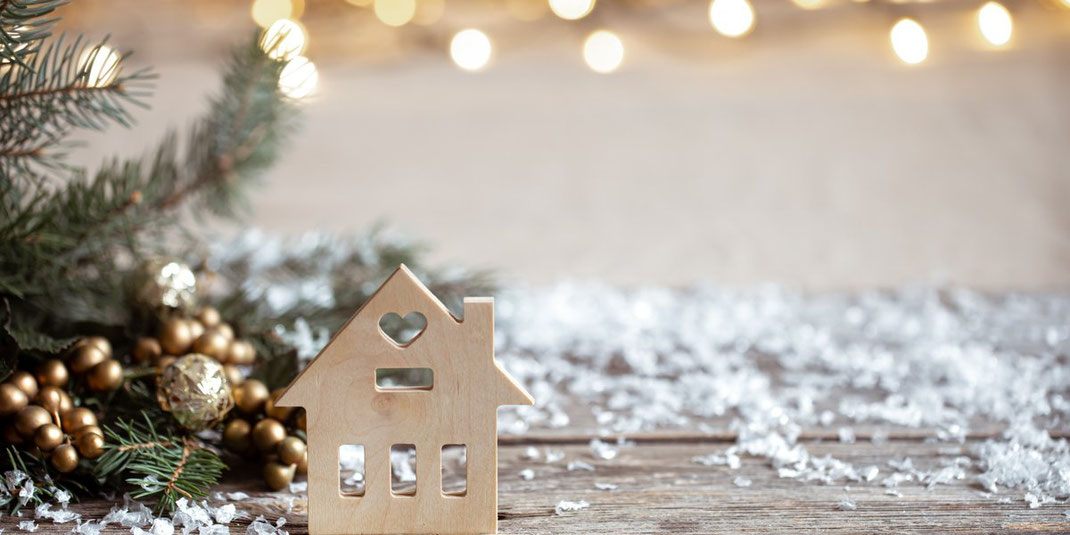 Kleines Holzhaus mit Herzfenster steht auf Holztisch mit Tannenzweigen und Weihnachtsdeko.