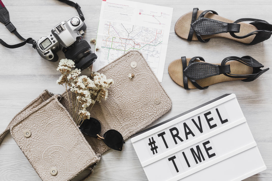 Flache Reise-Komposition mit Kamera, Sandalen, Karte, Handtasche und Leuchtbox mit #TravelTime – Urlaubsvorfreude und Reisezubehör für den Sommertrip