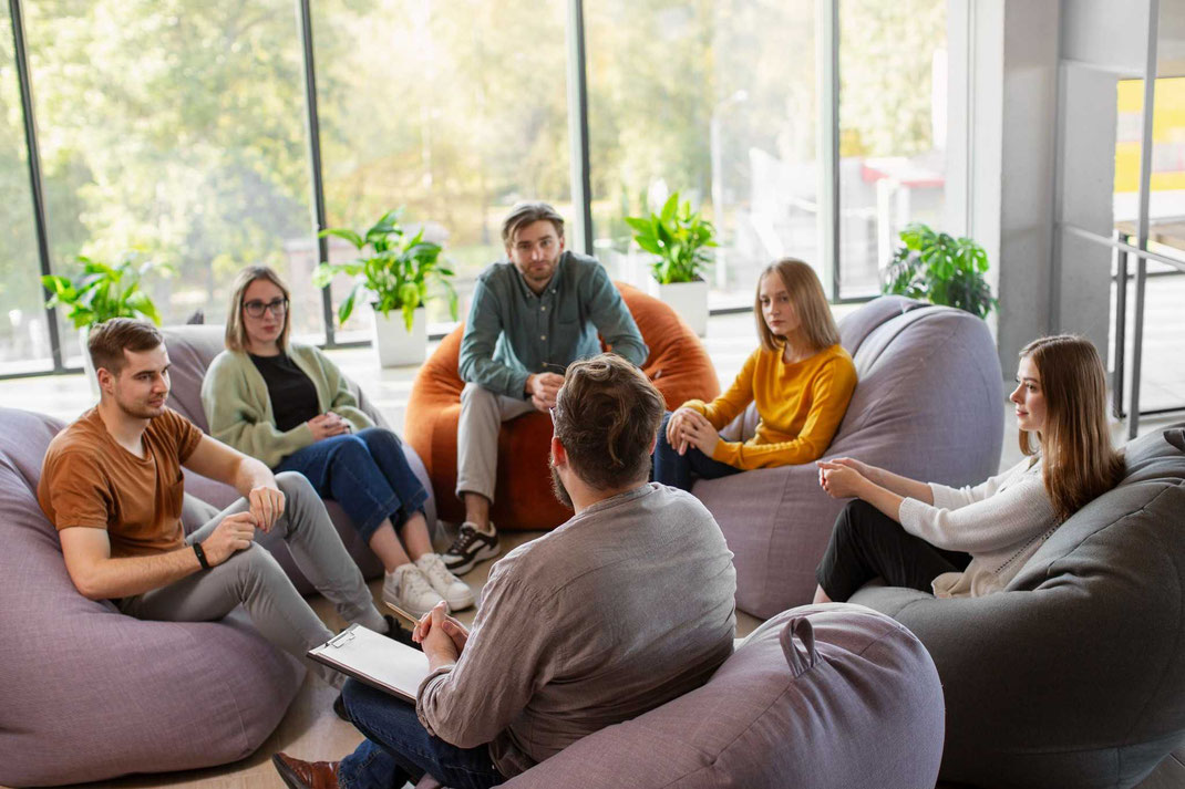 Gruppe junger Menschen sitzt in entspannter Atmosphäre auf Sitzsäcken und nimmt an einer Therapiesitzung teil.