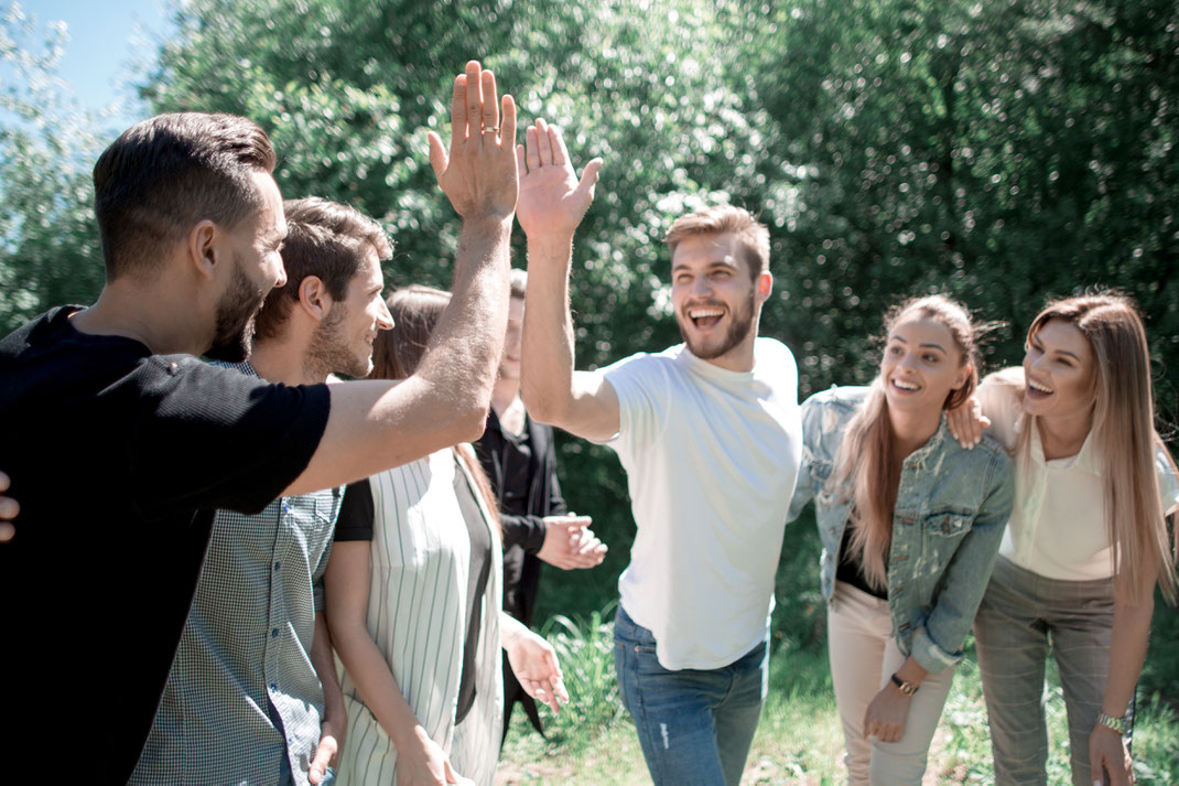 Gruppe junger Erwachsener feiert im Freien mit einem High-Five-Moment – ausgelassene Stimmung bei einem sonnigen Teamevent oder Freundetreffen.