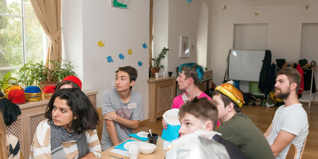 Junge Leute sitzen gemeinsam an einem Tisch bei einem Gruppenspiel oder Workshop in einem hellen Raum.