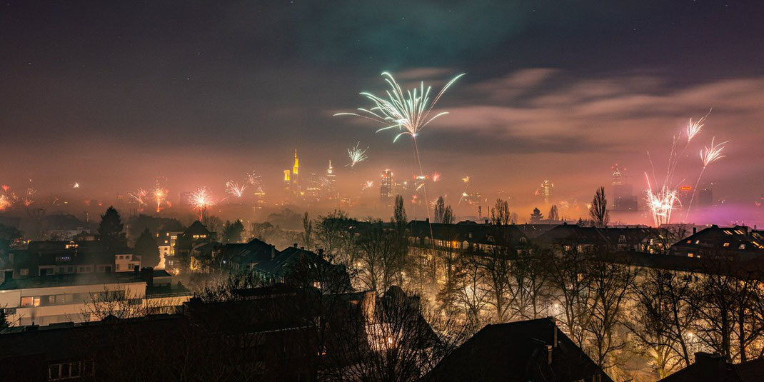 Blick auf eine Stadt mit Feuerwerk am Nachthimmel und beleuchteten Gebäuden.
