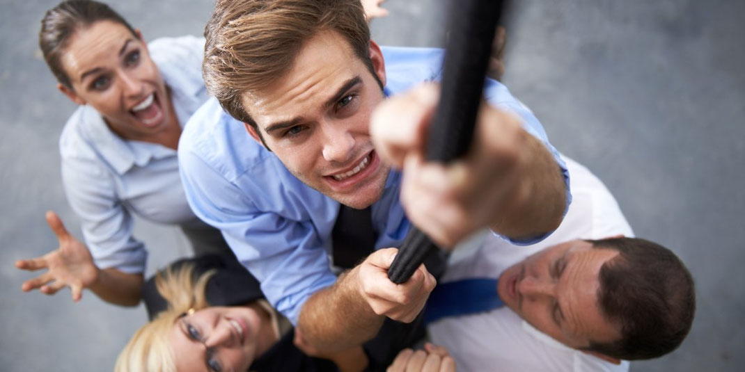 Team unterstützt Kollegen, der an einem Seil hochklettert, als Symbol für Zusammenhalt und Motivation.