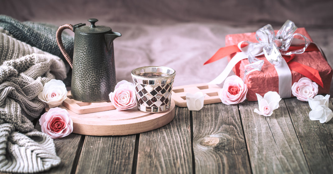 Romantisches Stillleben mit Geschenk, Rosen, Teekanne und Strickdecke auf Holztisch – Geschenkidee, Wohlfühlatmosphäre und Valentinstag-Inspiration